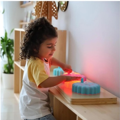 Criança a brincar com brinquedo educativo iluminado sobre mesa de madeira
