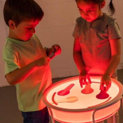 Crianças usando mesa iluminada com objetos coloridos em luz vermelha