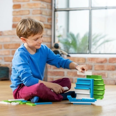 Menino a brincar com blocos de construção coloridos no chão em ambiente com paredes de tijolos.