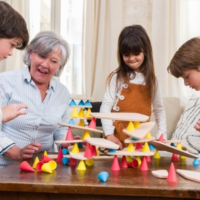 Jogo de construção de madeira com tábuas e cones coloridos numa mesa com pessoas ao redor