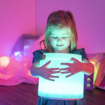 Menina com luminária portátil a emitir luz azul numa sala com iluminação roxa.