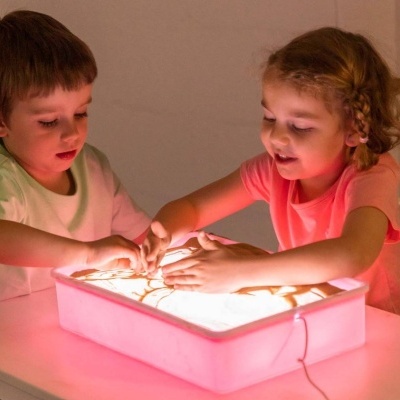 Caixa de luz retangular com laterais cor-de-rosa e crianças a brincar com areia
