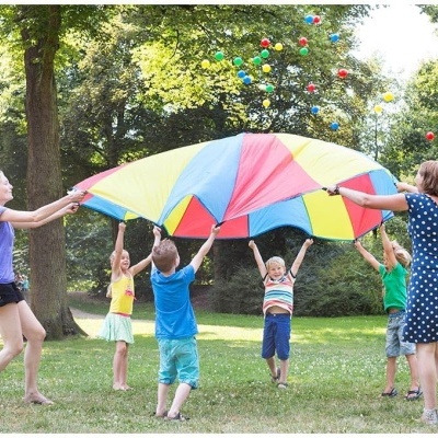 Crianças e adultos a brincar com tecido colorido num parque