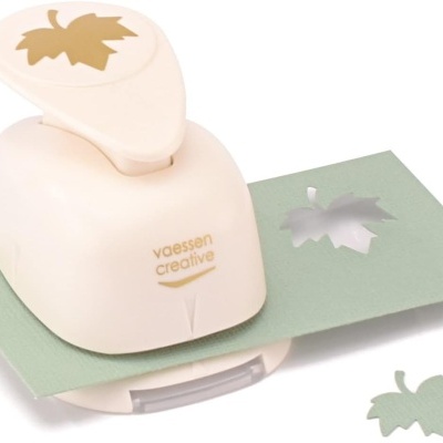 Perfurador de papel creme com desenho de folha de bordo, sobre papel verde com recorte da folha.