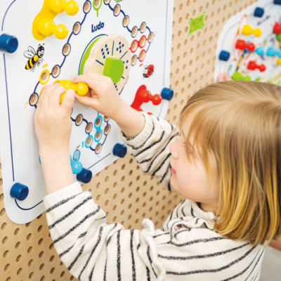 Jogo de Ludo infantil colorido fixado em parede de madeira com criança a jogar