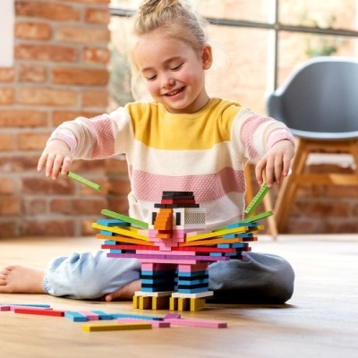 Menina a brincar com blocos coloridos formando um pássaro no chão de madeira