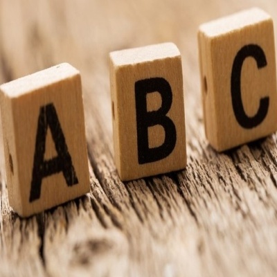 Três peças de madeira tipo Scrabble com as letras A, B e C em preto sobre madeira