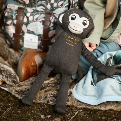 Boneco de peluche macaco preto com cara branca e detalhes amarelos perto de criança e mochila azul