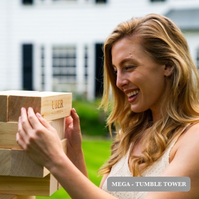 Mulher sorridente a jogar jogo MEGA - TUMBLE TOWER de madeira ao ar livre.
