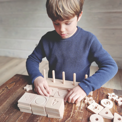 Menino a brincar com brinquedo de madeira com números e formas geométricas