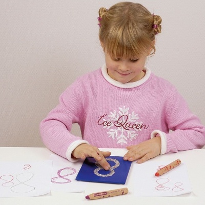 Criança com camisola rosa a desenhar com lápis coloridos numa mesa branca