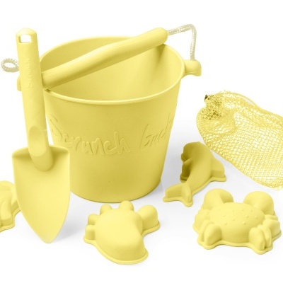 Conjunto amarelo de brinquedos de areia com balde, pá e moldes de animais e concha, com saco de rede amarelo.
