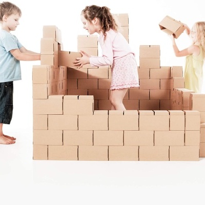 Crianças a brincar com blocos de cartão castanho claro, montando uma estrutura.
