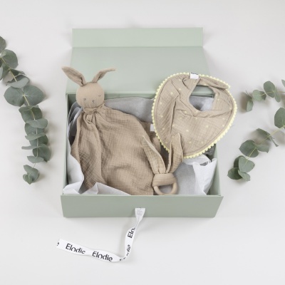 Conjunto de presente para bebé com brinquedo de coelho, bandana bege e anel de madeira numa caixa verde clara.