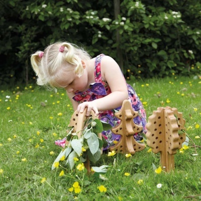 Menina a brincar com figuras de madeira em forma de árvores na relva