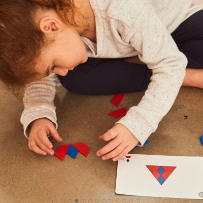 Criança a jogar com peças geométricas e uma carta com um padrão triangular colorido.