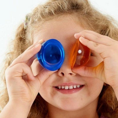 Criança segurando objetos redondos azul e laranja perto dos olhos