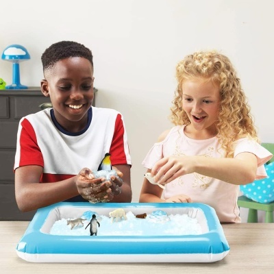 Crianças a brincar com tabuleiro inflável azul com gelo falso e animais do Ártico em mesa de madeira