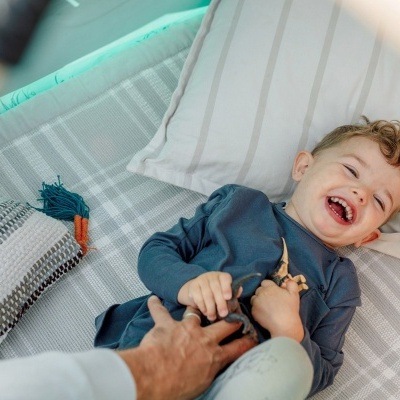 Menino a rir deitado num berço com colchão xadrez e almofadas coloridas