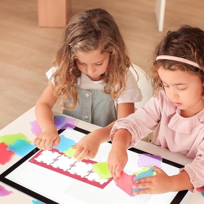 Duas meninas a brincar com peças de papel colorido numa mesa branca