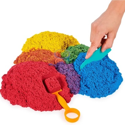 Montes de areia cinética colorida com pás de plástico e uma mão a mexer a areia azul