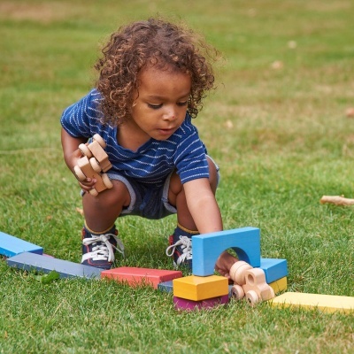 Criança brincando com blocos coloridos de madeira na relva