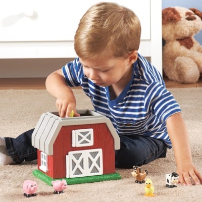 Menino a brincar com casa de brinquedo vermelha e animais de plástico num quarto com carpete bege
