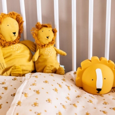 Brinquedos de leão amarelos numa cama de berço com lençóis estampados