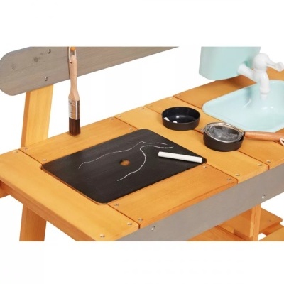 Bancada de madeira com tabuleiro preto, giz branco, pincel, potes pretos e pia azul com torneira branca