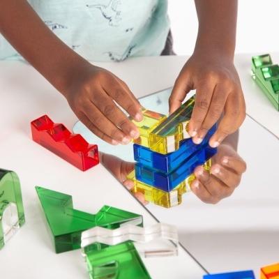 Criança empilhando blocos de plástico colorido sobre um espelho numa mesa branca
