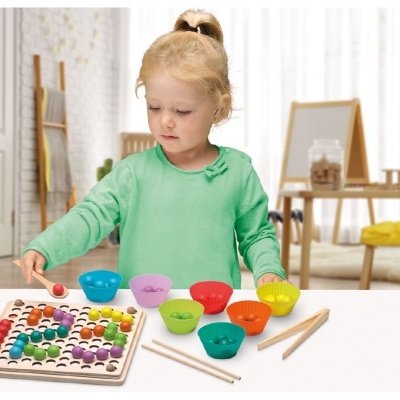 Criança a brincar jogo de madeira colorido com pinos e recipientes na mesa