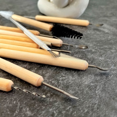 Ferramentas de escultura com cabos de madeira e pontas metálicas variadas sobre superfície cinza