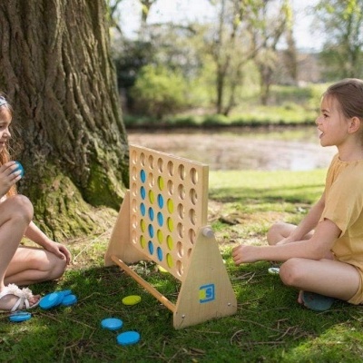 Duas raparigas a jogar jogo de tabuleiro ao ar livre junto a uma árvore e lago