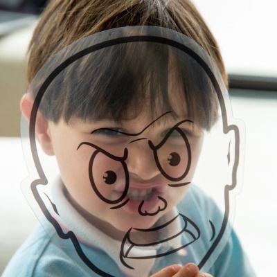 Criança sorridente com desenho de expressão de raiva num vidro