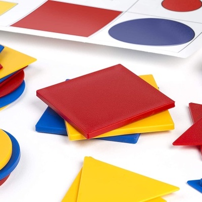 Peças geométricas coloridas em plástico vermelho, amarelo e azul sobre superfície branca