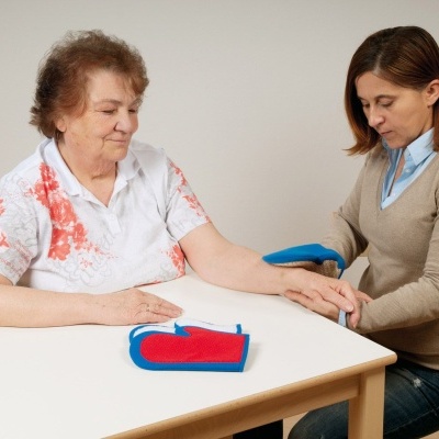Duas mulheres sentadas à mesa usando almofadas vermelho e azul, uma segura o pulso da outra.