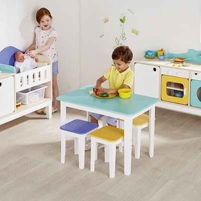 Conjunto infantil de mesa, bancos e mobiliário de brincar em cores azul claro, amarelo, branco, com crianças a interagir
