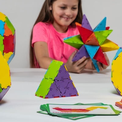 Brinquedos de construção geométrica coloridos em plástico com criança a brincar ao fundo