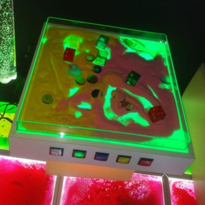 Caixa de areia sensorial iluminada com objetos coloridos e botões multicolor na base branca