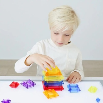 Criança empilhando figuras geométricas coloridas em acrílico sobre mesa iluminada
