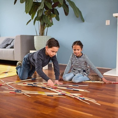 Crianças a jogar com pauzinhos coloridos em chão de madeira numa sala de estar