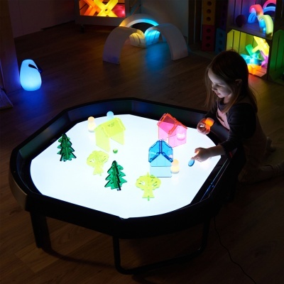 Mesa de luz octogonal com peças coloridas translúcidas e criança a brincar