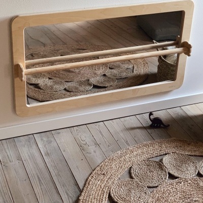 Espelho de parede com moldura e barras de madeira em ambiente com chão e tapete de madeira e fibras naturais