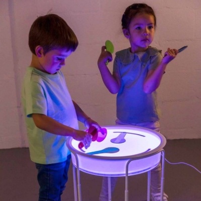 Mesa redonda iluminada com duas crianças a brincar com objetos coloridos