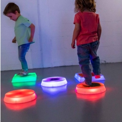 Crianças em cima de blocos iluminados coloridos num chão cinza