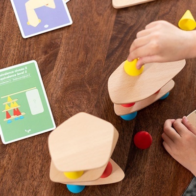 Jogo de equilíbrio infantil com peças de madeira coloridas e cartas de jogo numa mesa de madeira.