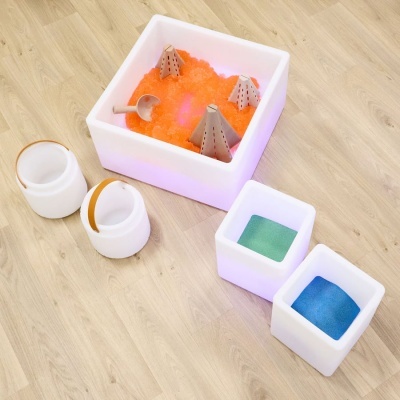 Recipientes brancos em plástico translúcido com gel laranja e areia colorida sobre chão de madeira