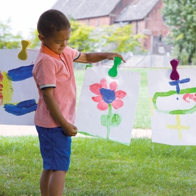 Menino pendura desenhos coloridos num estendal ao ar livre com presilhas de plástico
