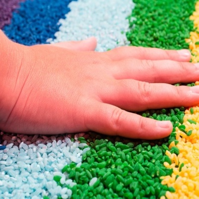 Mão sobre grânulos plásticos coloridos organizados em faixas