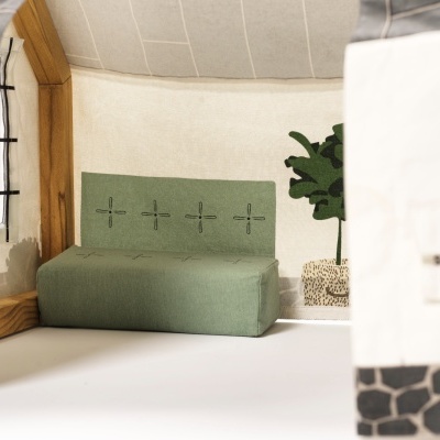 Interior de casa de brinquedo com sofá verde e planta decorativa.